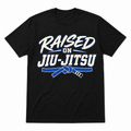 A black short-sleeve crewneck t-shirt featuring a graphic print on the front that reads 'RAISED ON JIU-JITSU' in white and blue lettering, with a blue martial arts belt tied in a knot below.