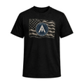 A black short-sleeve crewneck t-shirt featuring a distressed graphic of a waving American flag with a circular emblem in the center containing a stylized letter 'A' and the words 'TEAM ALPHA'.