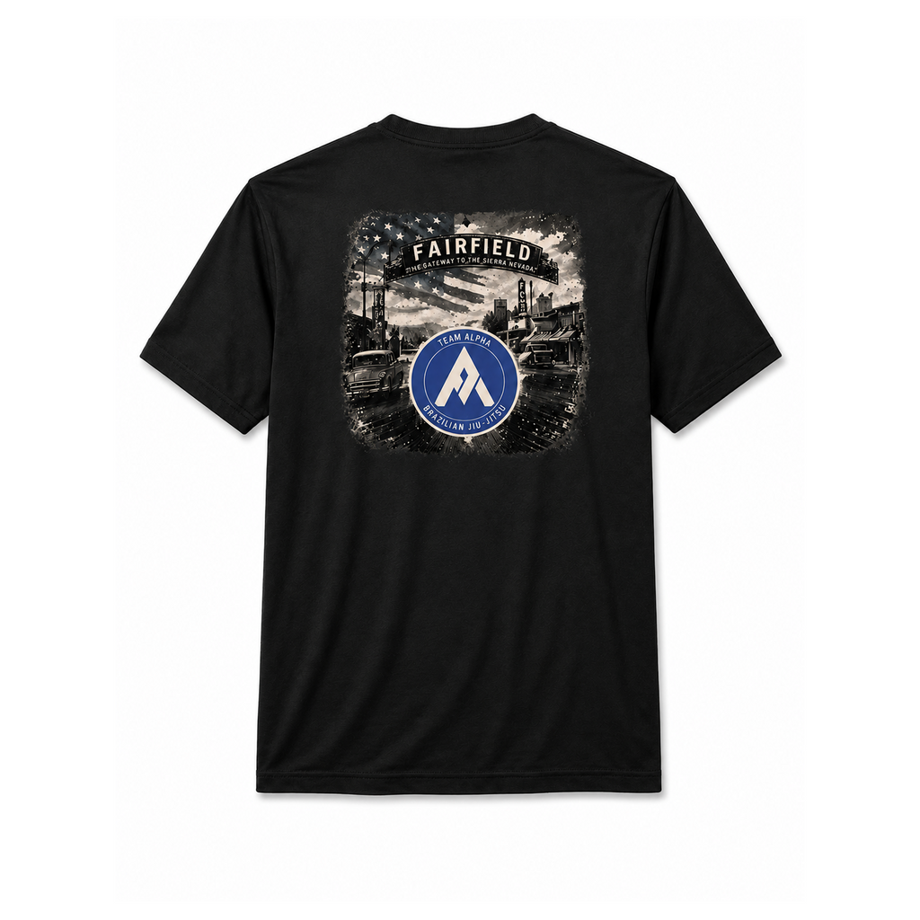 A black short-sleeve t-shirt shown from the back, featuring a large graphic print with the word 'FAIRFIELD' above a monochrome industrial scene and a blue circular emblem with a white 'A' and the text 'TEAM ALPHA'.