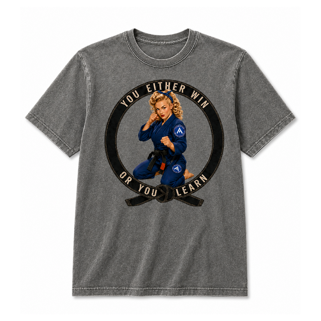 A gray acid-wash t-shirt featuring a circular graphic of a Brazilian Jiu-Jitsu (BJJ) woman in a blue gi with a black belt. The graphic includes the text 'YOU EITHER WIN OR YOU LEARN' in beige.